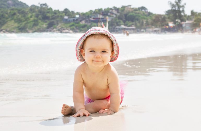 Beba na plaži nosi na glavi šeširić.